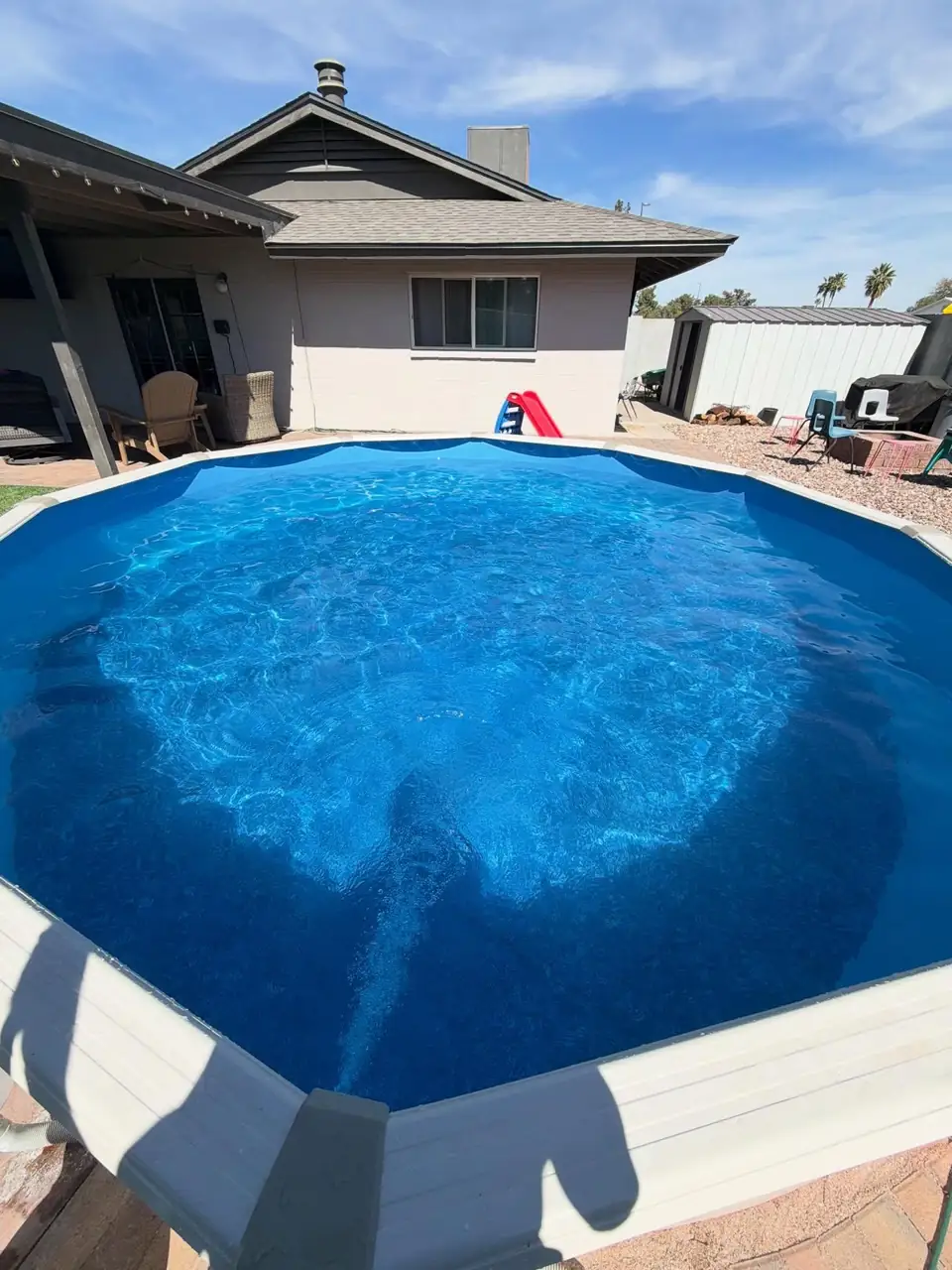 A round backyard pool with deep blue water beside a stucco house