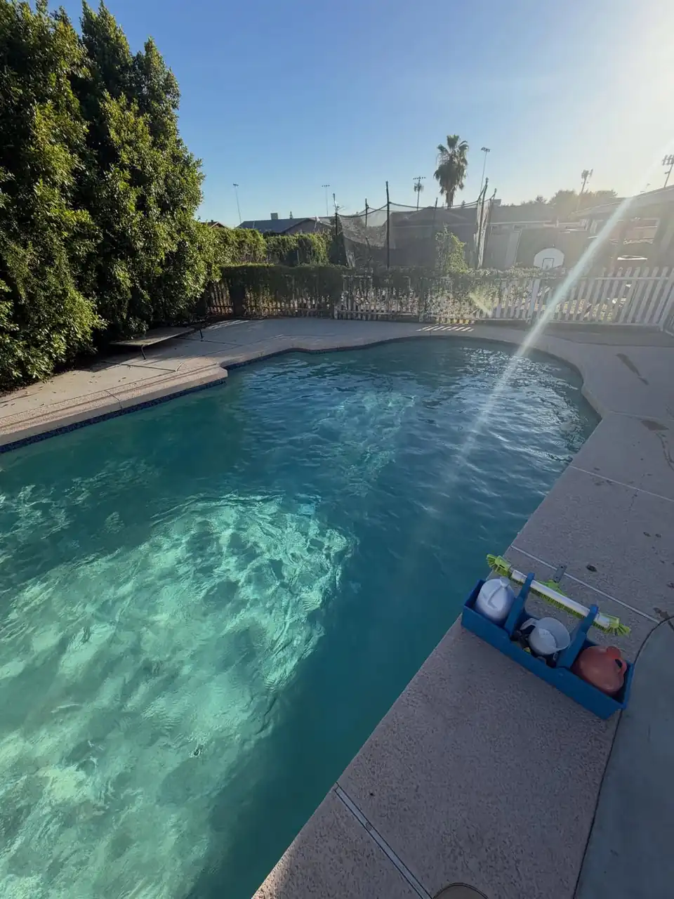 A sunlit pool with clear water and a test kit on the deck