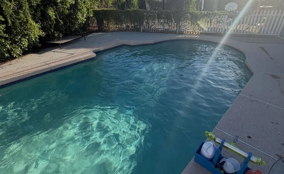 A sunlit pool with clear water and a test kit on the deck