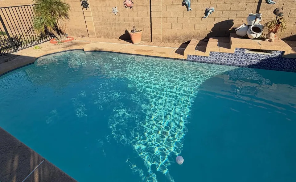 A clear blue backyard pool with a pool brush on its pole along the deck