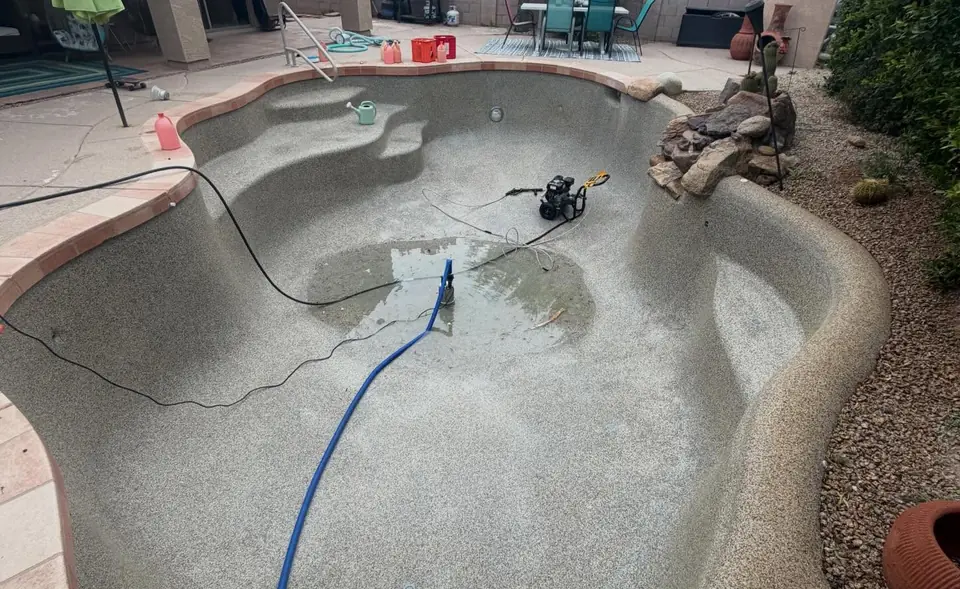 A drained pool with a hose and pump on the bare plaster floor