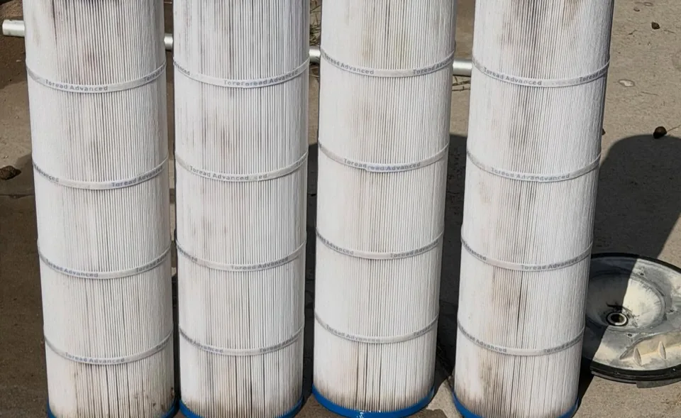Four pool filter cartridges, cleaned white, standing on a concrete pad