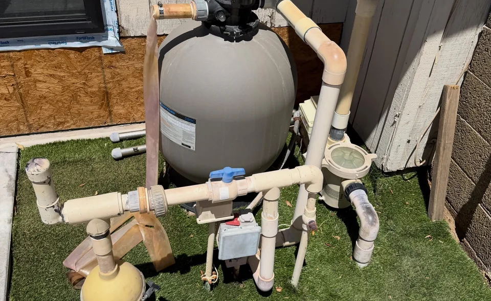A sand filter, pump and white plumbing valves on a pool equipment pad