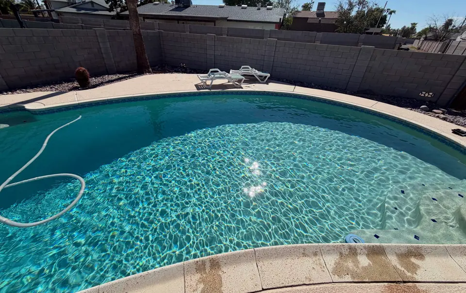 A backyard pool with clear, sparkling water and a cleaning hose along the floor