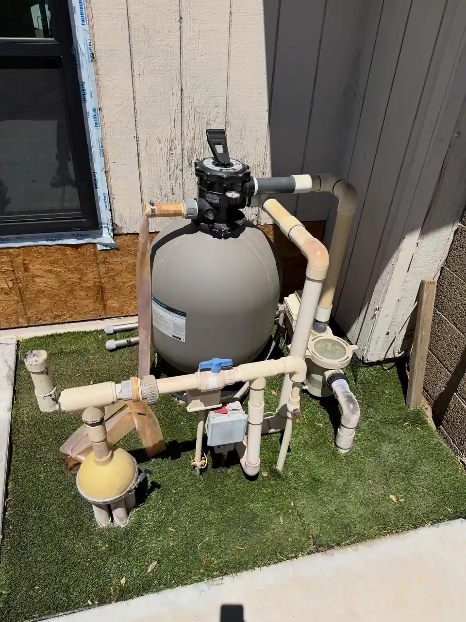 A sand filter, pump and white plumbing valves on a pool equipment pad