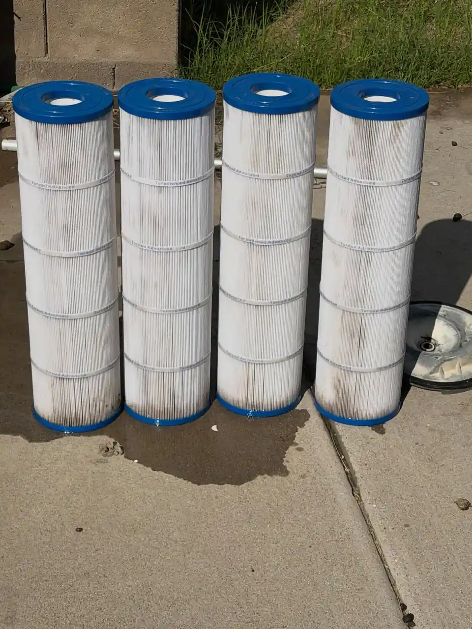 Four pool filter cartridges, cleaned white, standing on a concrete pad